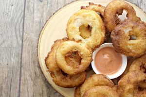 A plate of Old Fashion Onion Rings with a small bowl of dipping sauce.