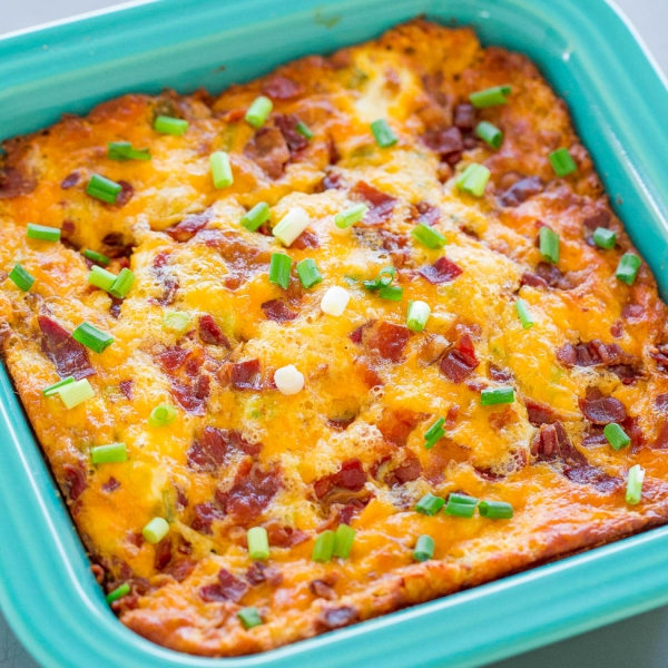 A Bacon, Cheddar and Egg Casserole topped with green onions in a casserole dish.