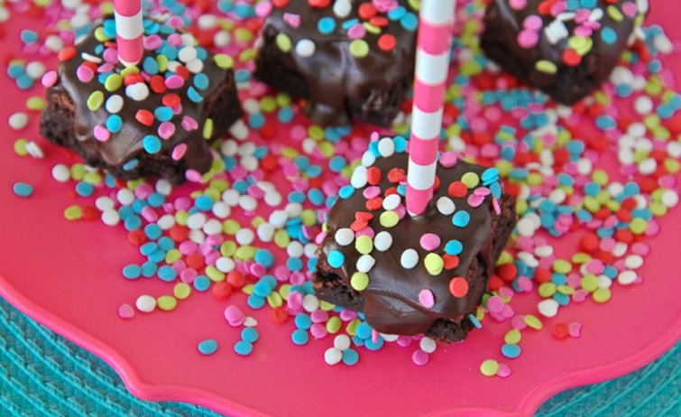 Several Gluten Free Chocolate Covered Brownie Bites topped with multi-colored sprinkles on a pink plate.