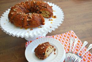 A Nutty Banoffee Bundt Cake on a cake platter with a slice cut out and that slice placed on a small plate off to the side.