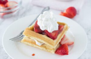 Two Coconut Waffles with Compote topped with whipped cream and strawberries.