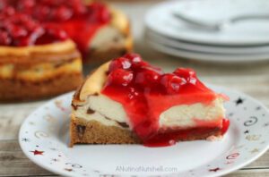 A slice of Cherry Topped Cheesecake with Triple Chocolate Chunk Cookie Crust topped with a cherry pie filling.