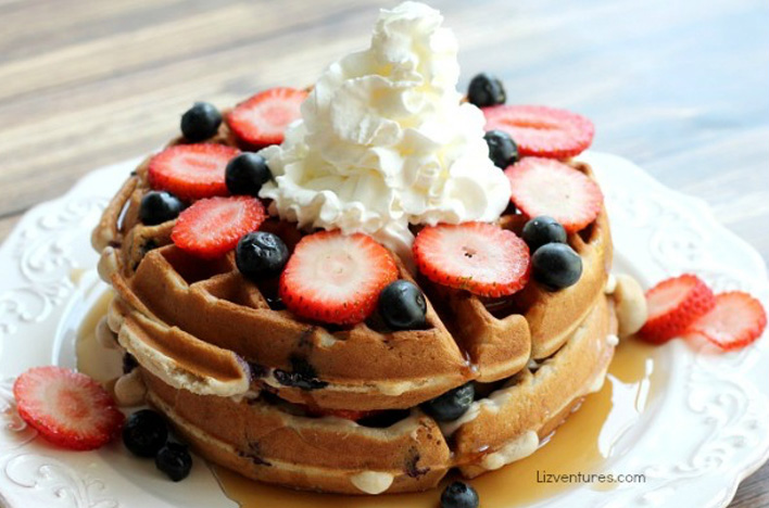 A stack of Mixed Berry Cream Cheese Waffle Cakes topped with strawberries, blueberries and whipped cream.
