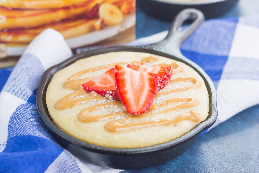 A Peanut Butter and Jelly Baked Pancake in a skillet topped with peanut butter syrup and strawberry slices.