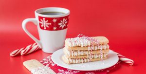 A plate of Peppermint Crunch Sugar Cookie Sticks with candy cane garnish and a mug of coffee.