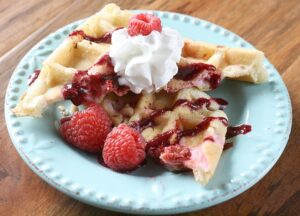 A Raspberries and Cream Stuffed Waffle topped with whipped cream and raspberries.