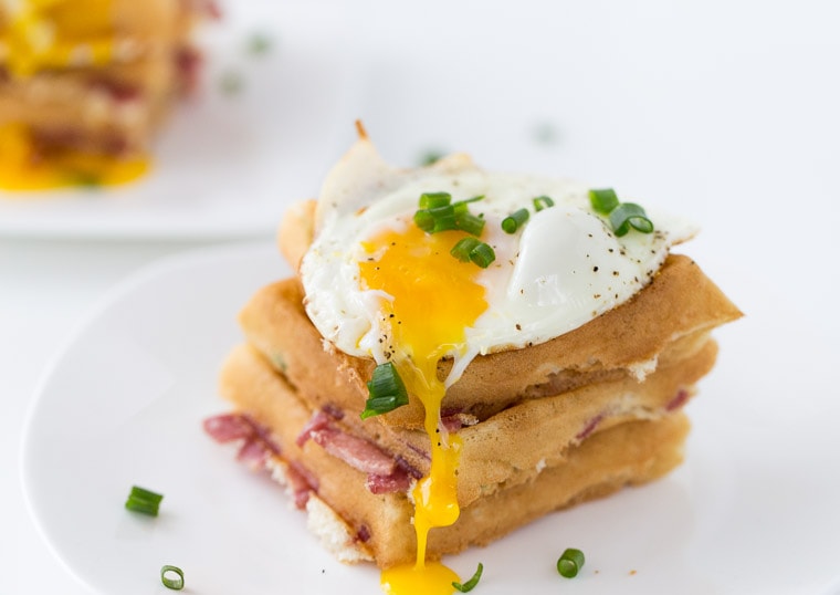A stack of Savory Breakfast Waffles topped with a sunny side up egg and scallions.