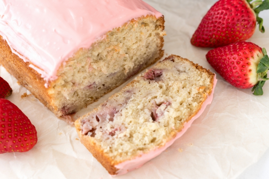 A loaf of Strawberry Banana Bread with a slice cut and strawberries on the side.