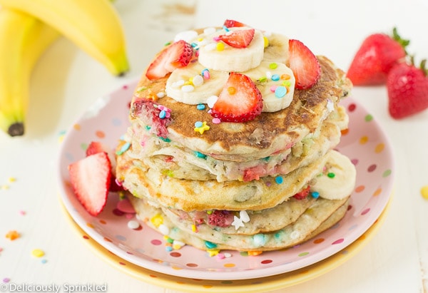 A stack of Strawberry Banana Protein Pancakes topped with sliced strawberries, bananas and sprinkles.