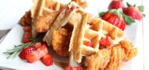 A plate full of Strawberry and Rosemary Chicken and Waffles with strawberries as garnish.