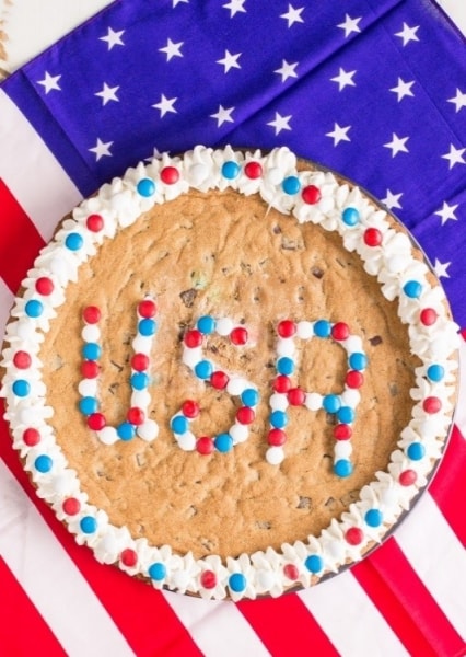 A USA Chocolate Chunk Cookie Cake with vanilla frosting and red, white and blue colored chocolate candies spelling "USA".