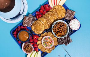 A blue charcuterie board filled with Krusteaz buttermilk pancakes, slice fruit, nuts, and other fun toppings.