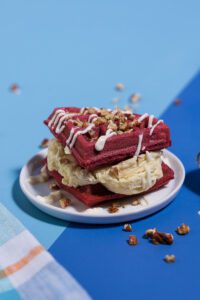 A Red Velvet Ice Cream Sandwich topped with a cream cheese drizzle and chopped pecans.