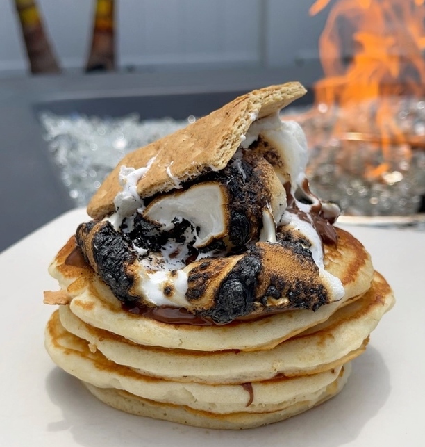 A stack of S'mores Pancakes topped with a gooey marshmallow and graham cracker.