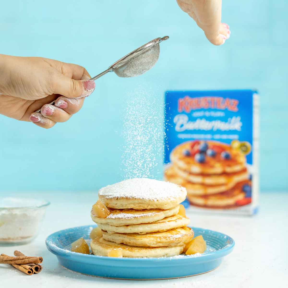 A stack of buttermilk pancakes being sprinkled with an Apple Cider Sugar Pancake Topping.
