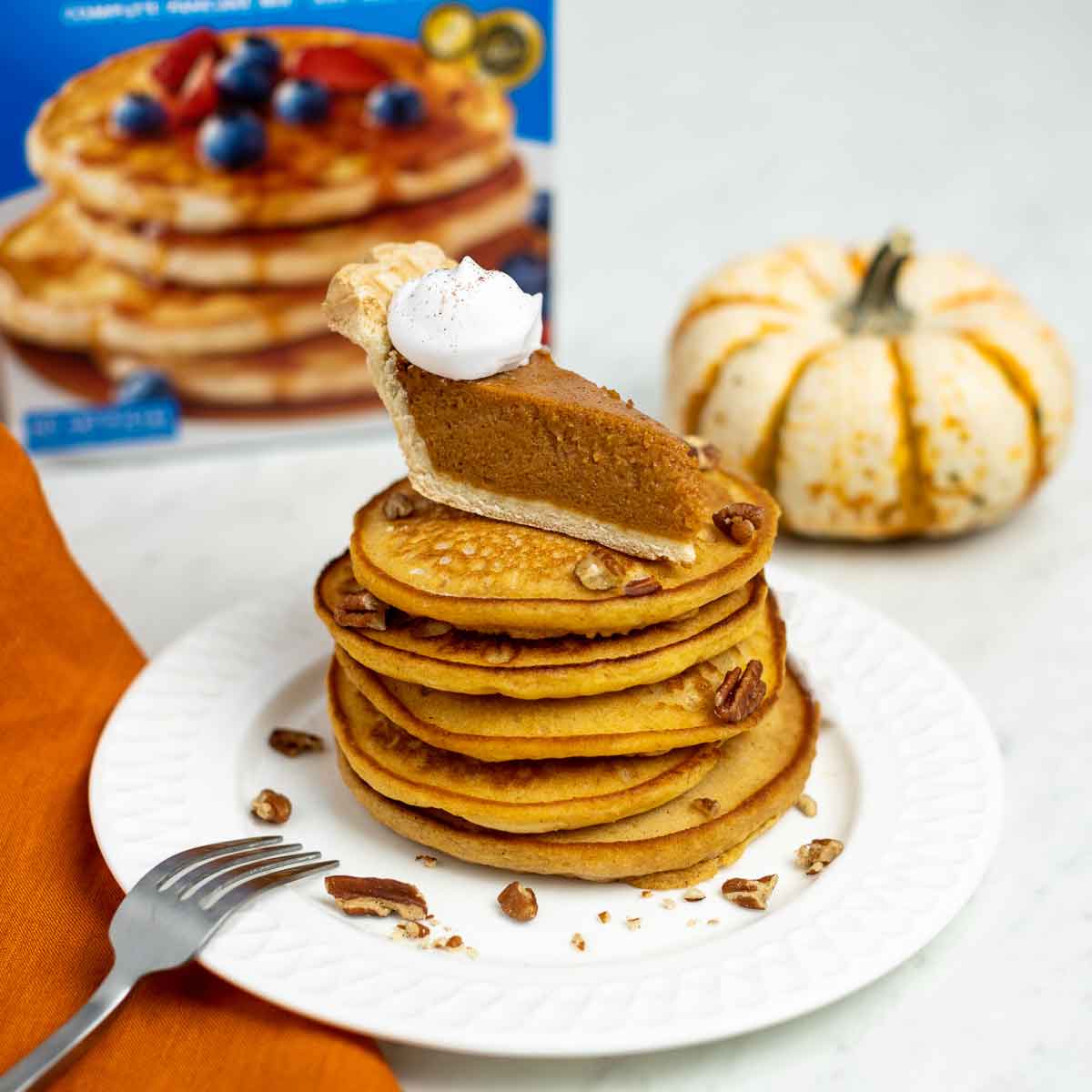 A stack of Pumpkin Pie Pancakes topped with a slice of pumpkin pie and chopped pecans.