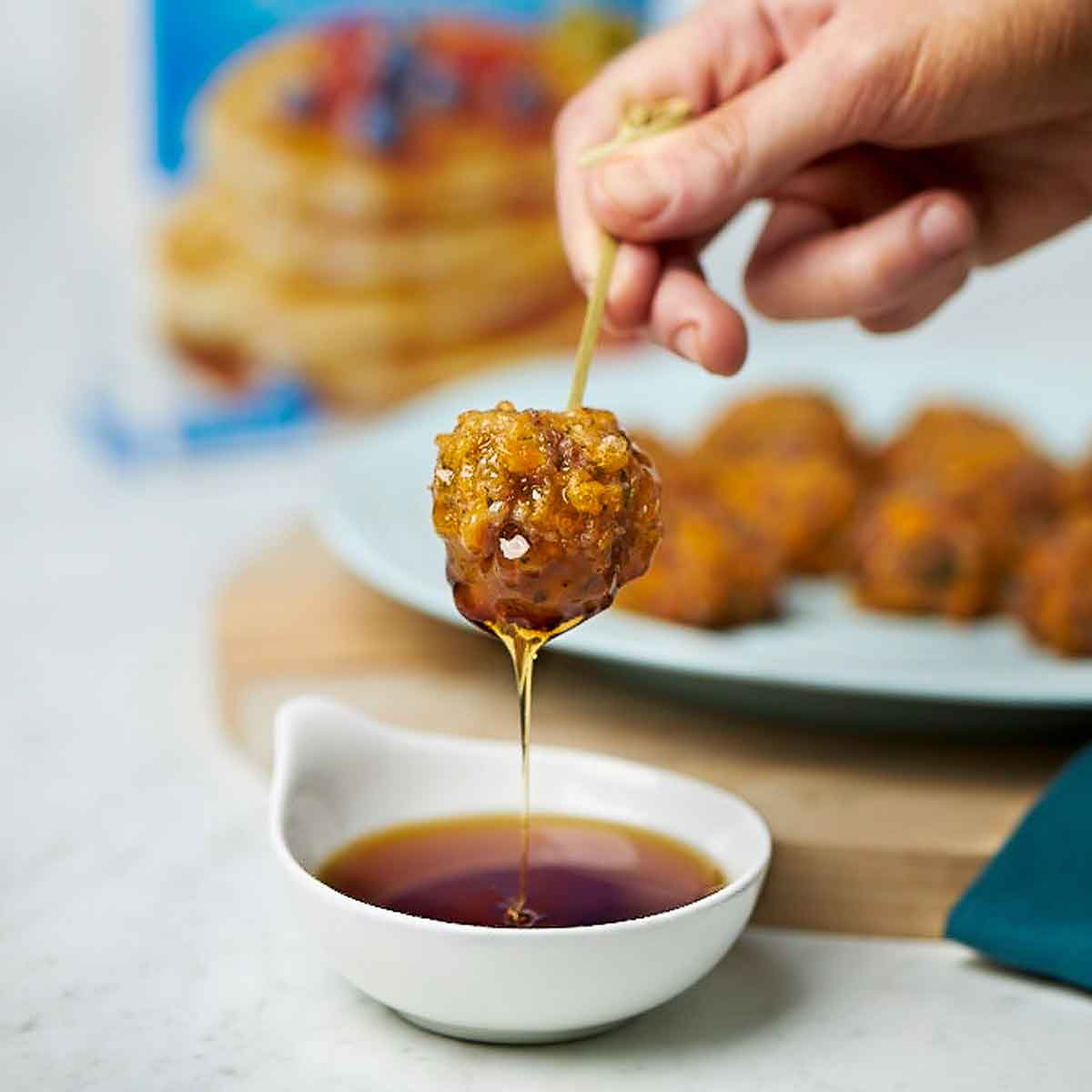 A Sausage Ball stuck with a toothpick being dipped in syrup.
