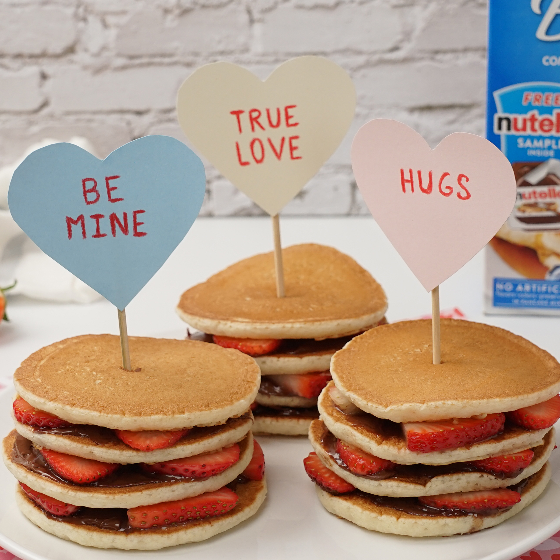 Three stacks of Strawberry Nutella® Mini Stacks with layers of Nutella® and strawberries. In each stack of pancakes is a heart shaped decoration.