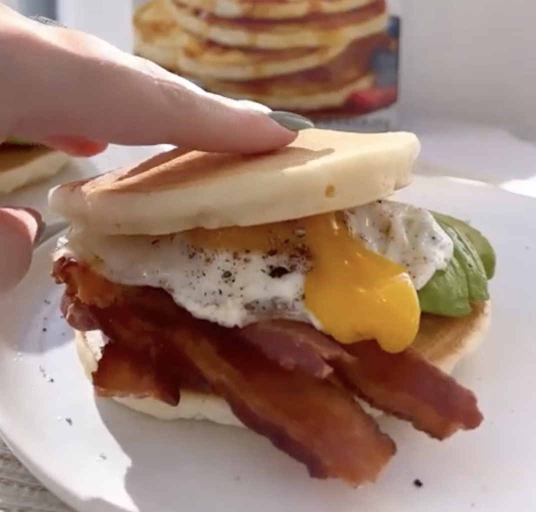A Bacon Pancake Breakfast Sandwich being gently pressed on so the egg yolk runs out slightly.