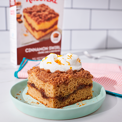 A plate of Spiced Chai Crumb Cake topped with whipped cream and orange zest.