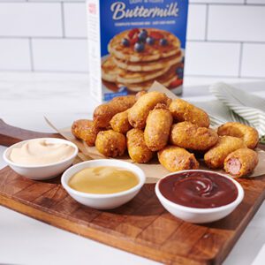 A batch of Homemade Mini Corndogs on a serving platter paired with three different dipping sauces.