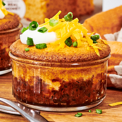 A Chili Cornbread Pot Pie topped with cheese, chives and sour cream in a small ramekin.