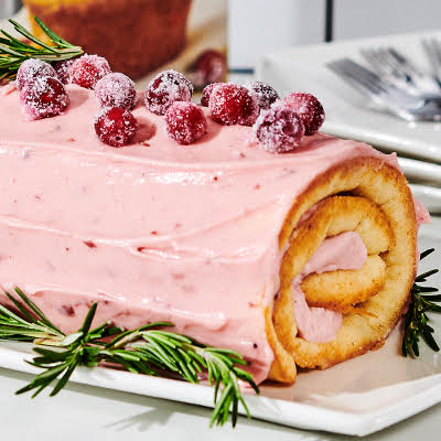 A Cranberry Orange Jelly Roll garnished with sugared cranberries and rosemary.