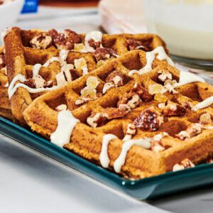 Gingerbread Waffles laid out on a platter and topped with melted white chocolate and candied pecans and ginger.