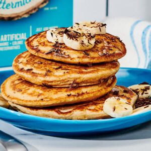A stack of Stuffed Protein Pancakes topped with banana slices and chocolate shavings.