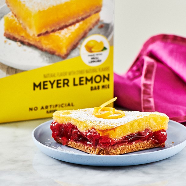 A Cherry Filled Lemon Bar topped with powdered sugar and a lemon shaving.