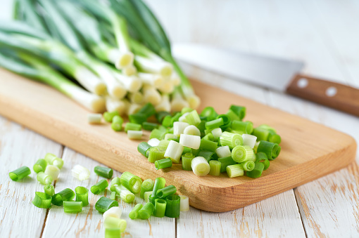 Heap of chopped green onion on a wooden cutting board , selective focus.