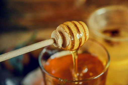 Close up of honey on a wooden spoon for honey, dripping from a spoon.