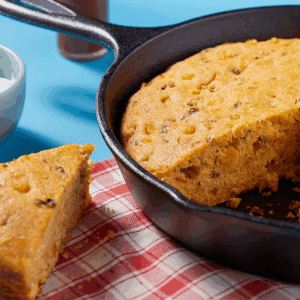 A slice of cheesy green onion and double cornbread next to a skillet full of it