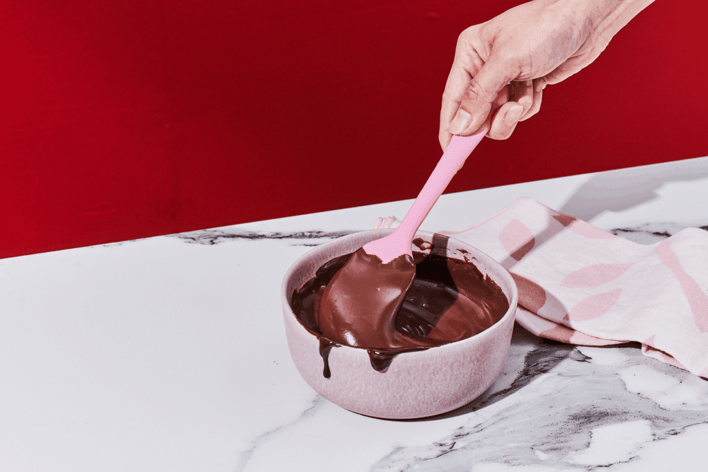 Chocolate glaze frosting being stirred in a bowl.
