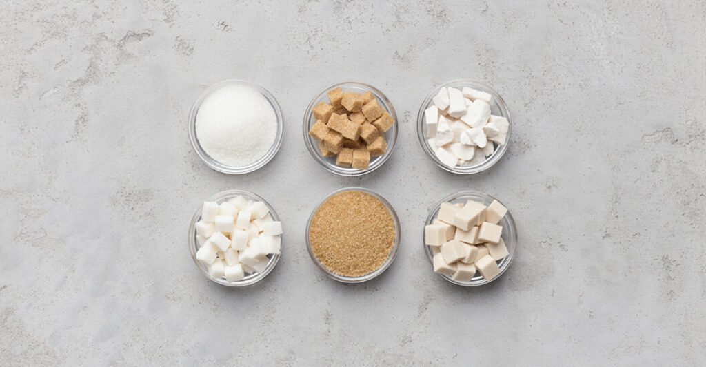 Six different types of sugars sitting in a circular jars on a stone countertop
