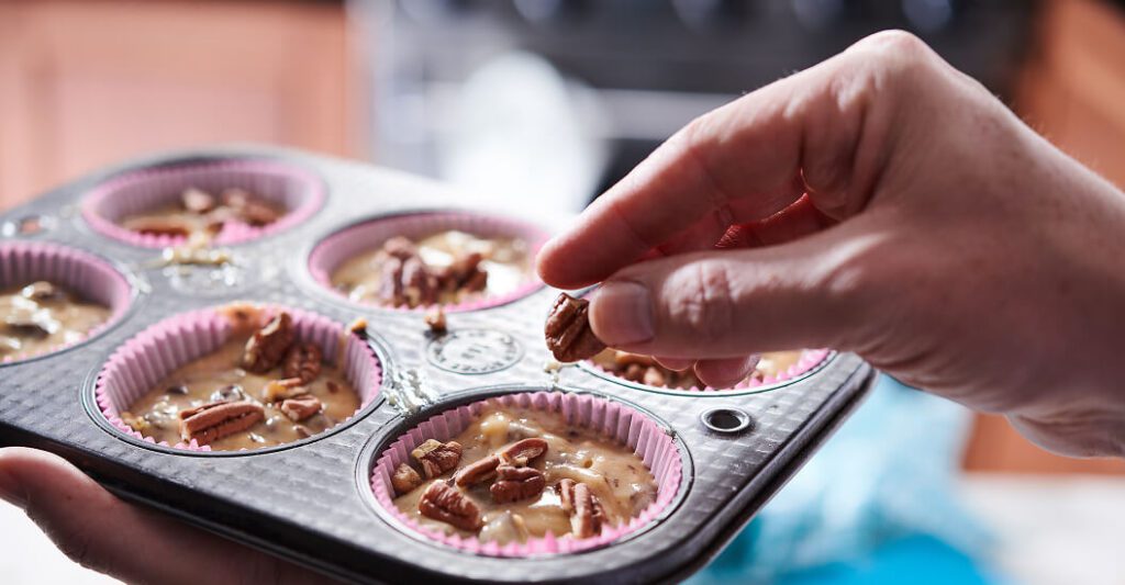 Woman's hand spreading nuts into a muffin tin